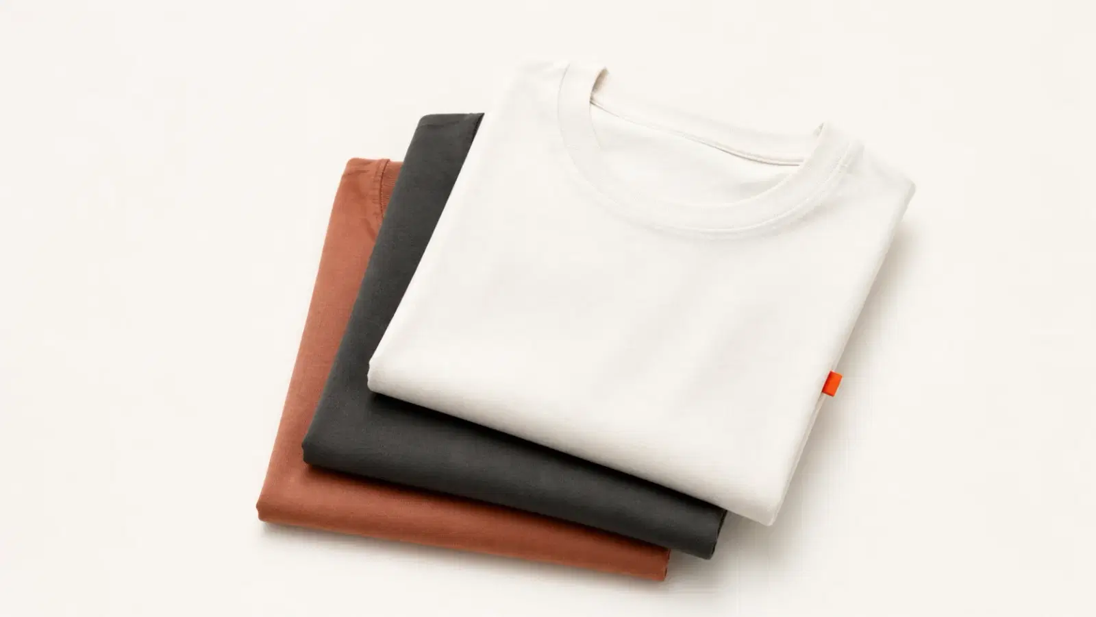 Stacked blank t-shirts in different fabric weights and colors laid out on a clean studio surface, representing the best blank tees for a print-on-demand clothing brand.